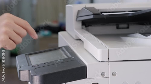 Close-up of person operating modern office copier by pressing touchscreen panel and making photocopies. Office workflow, technology, document management in professional environment