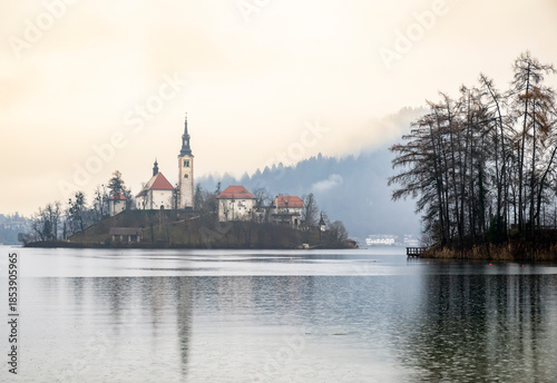 calm lake scene with a small island featuring a church surrounded by foggy forest trees