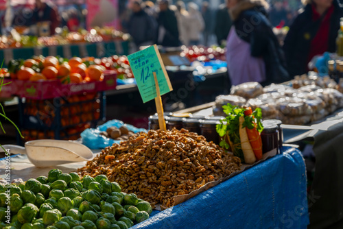 fresh walnuts and assorted vegetables displayed in busy outdoor market with vendors and customers