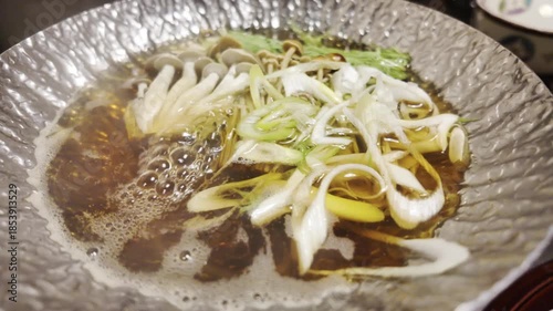 Water boils in a silver pot with various vegetables cooking inside.