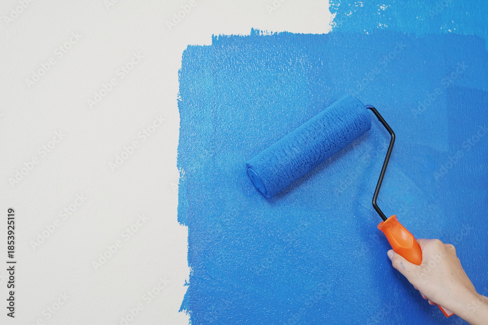 Obraz premium Roller Brush Painting, Worker painting on surface wall Painting apartment, renovating with blue color paint. Leave empty copy space white to write descriptive text beside. 