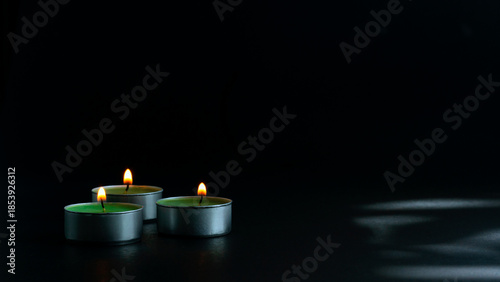 Multiple burning tealight candles arranged in a row against a dark background, symbolizing remembrance, peace, spirituality, unity, and calm atmosphere with copy space.