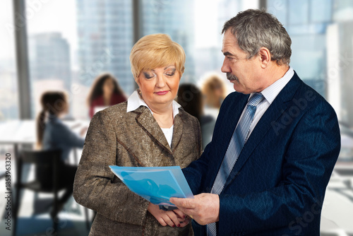 A man and a woman are looking at a blue piece of paper. The man is wearing a suit and tie