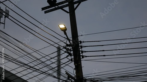 Dense tangle of utility wires and cables forming a busy silhouette around a wooden pole against a deep blue evening sky, urban electric infrastructure complexity.