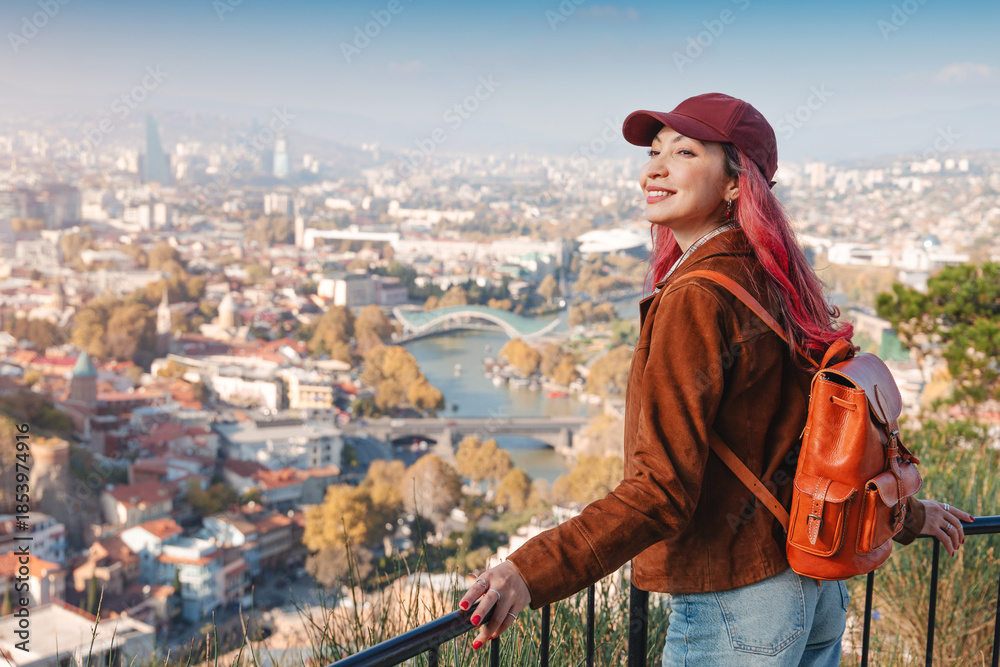 Fototapeta premium Woman with backpack admiring the panoramic cityscape of Tbilisi, Georgia, from a high viewpoint, experiencing travel and tourism