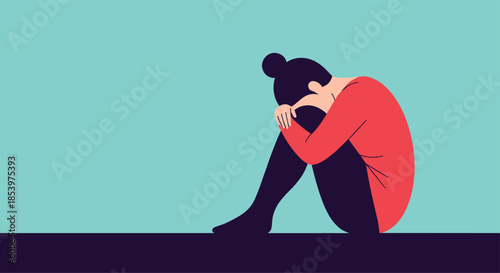 Sad woman sitting alone on the floor and hugging her knees in a state of depression, loneliness, or emotional distress against a teal background.