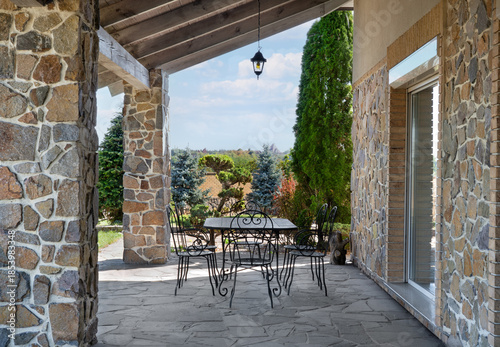 Billede på lærred Covered stone terrace with wrought iron garden furniture, rustic countryside hou