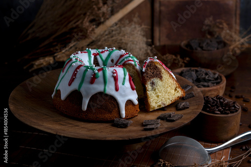 Vanilla and chocolate pudding covered with white sugar sauce, decorated with red and green icing and coffee beans in a kitchen with wood 