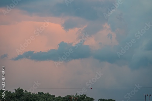 A sunset scene with a tumultuous cloud formation, contrasting dark grays and blues against soft pinks and purples Indistinct object or structure in lower right corner, adding intrigue Lighting prim