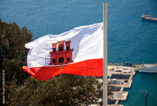 UK overseas - Gibraltar - The famous red castle with three towers and the gold key on the waving national Gibraltar flag with blurred sea and port background