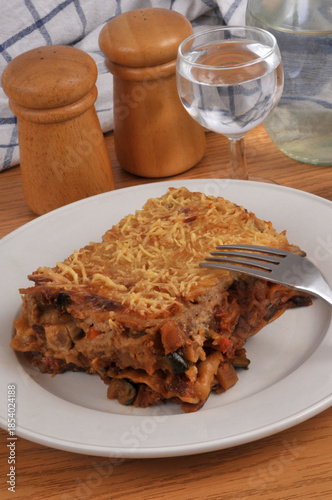 Part de lasagnes aux légumes maison servie dans une assiette avec une fourchette en gros plan servie à table avec un verre d'eau