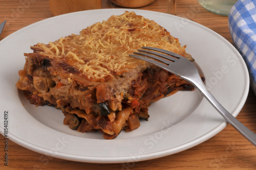 Part de lasagnes aux légumes maison servie dans une assiette avec une fourchette en gros plan servie à table