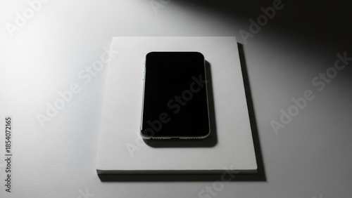Minimalist black smartphone resting on a white surface with dramatic lighting
