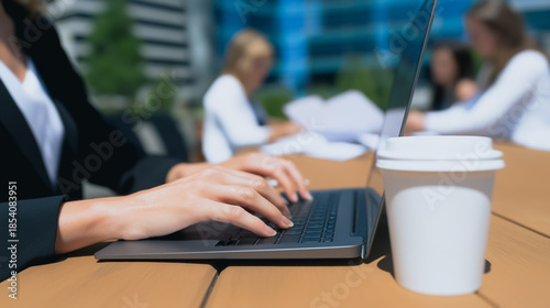 A businesswoman working on laptop, with focus on hands typing with a cup of coffee. The scene set on a outdoor desk.