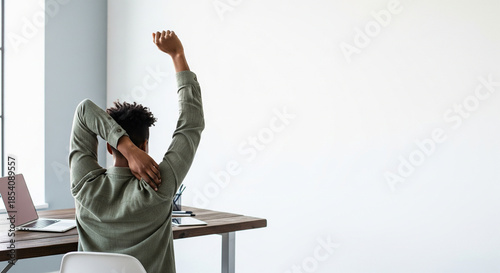 Rear view of young man stretching at minimalist home office desk with copy space