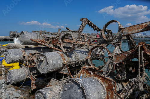 Rusty, barnacle-covered metal pipes at an abandoned harbor symbolize the environmental impact of industry on marine ecosystems.