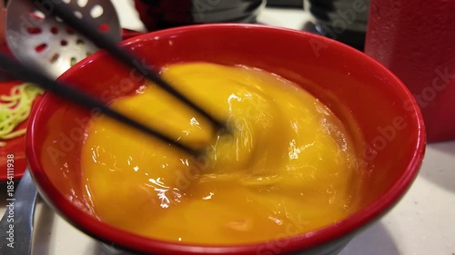 Chopsticks stirring raw egg in red bowl

