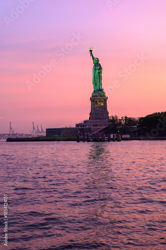 Statue of Liberty at sunset with pink sky. The Statue of Liberty stands against a vivid pink and orange sky at sunset.
