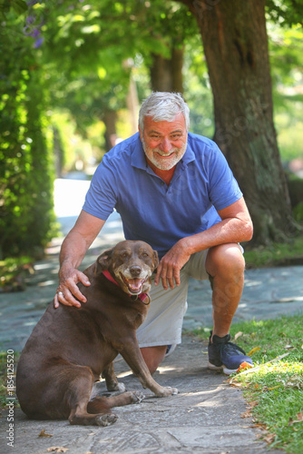 Portrait of a senior Latino man with his Labrador dog in a green park setting. The image conveys companionship, loyalty, wellbeing, and a calm outdoor lifestyle.