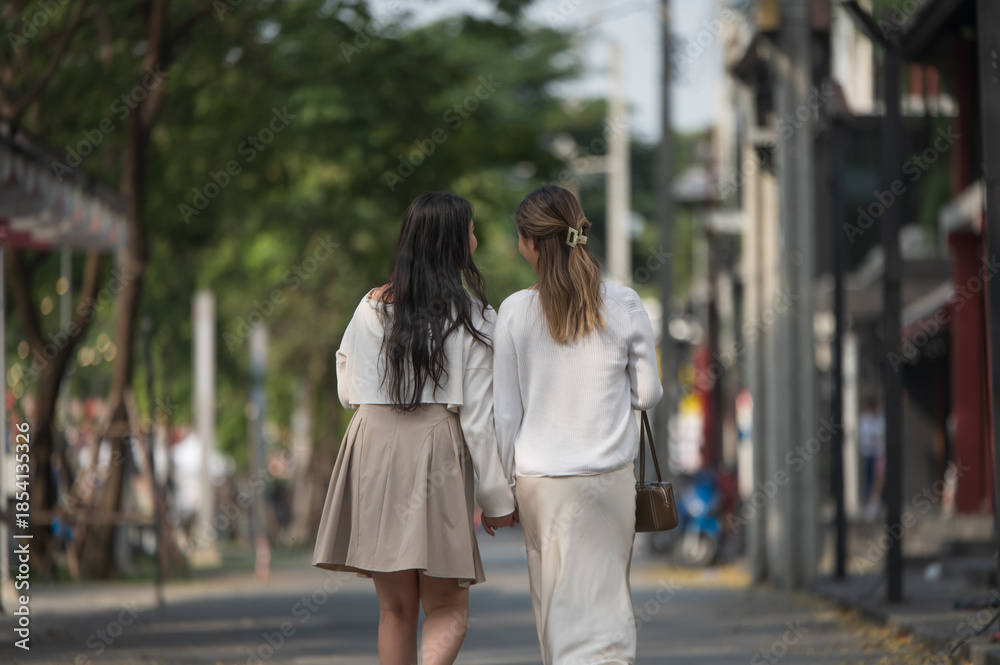 Naklejka premium Two young female friends walking hand in hand down a city street together.