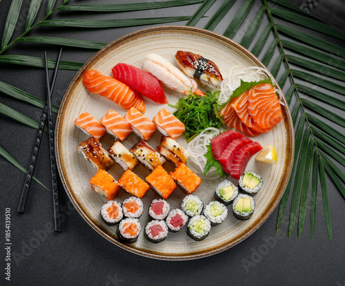 Sushi and Sashimi Platter with Rolls and Vegetables. A round platter displays an array of sushi, sashimi, and maki rolls, including tuna, salmon, and eel, with seaweed and vegetables.