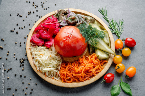 Assorted Fermented and Pickled Vegetables Appetizer Platter. A wooden platter displays an array of fermented and pickled vegetables, including cabbage, carrots, mushrooms, and a whole ripe tomato.
