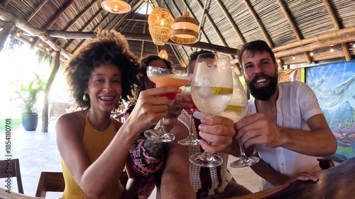 Diverse group of friends celebrating and clinking glasses with colorful cocktails. Happy people enjoying a party at a beach resort bar