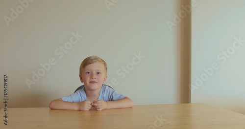 A young boy sits at a table, attentively listening and raising his hands. Learning process, discipline in class.