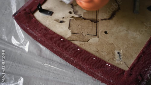 Close up of furniture restorer hands using pliers to remove old upholstery from vintage wooden chair