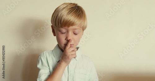 A close-up of a fair-skinned boy, thoughtfully putting his index finger to his lips and making a Shhh sound, then looking at the camera and smiling.