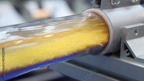 Plastic pellets air tubes. Close up of transparent industrial tube transporting yellow plastic pellets on automated machine. High speed motion engineering material handling. Plastic manufacturing tech