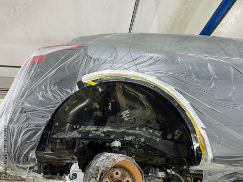 plastic sheeting encases wheel arch and sealed border to prevent dust spread, wheel arch protected by plastic cover with taped edges for contamination control during painting process