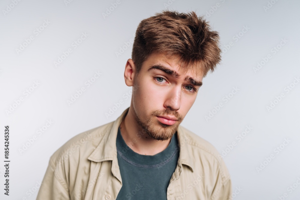 Fototapeta premium Young man with short hair and beard poses against a plain background in a casual setting during the daytime