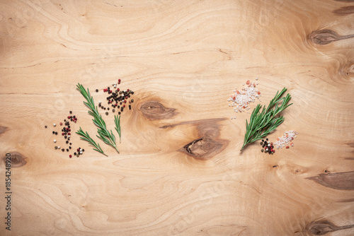Culinary background, rosemary sprigs, peppercorns and pink himalayan salt on on wooden plywood, flat lay, top view, copy space