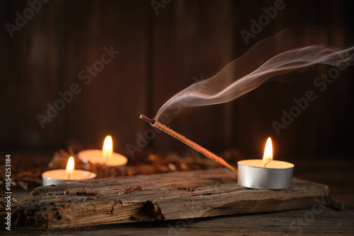 Incense Stick Releases Smoke Next to Candles on Wooden Surface at Night
