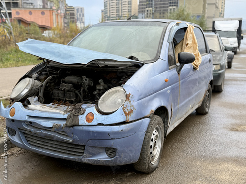 Old Neglected Vehicle Scene, Rusty Compact Vehicle With Broken Signals And Deflated Tire, Dilapidated Blue Hatchback Neglected Outside With Damaged Front And Worn Appearance