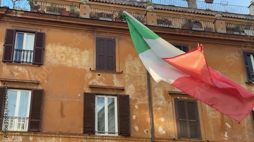 National Day of Italy.Close-up view of an Italian flag on a building balcony with ornate details and wooden shutters, captured in sunlight.