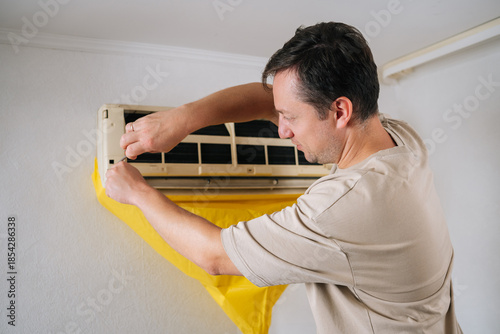 Photography Back view of HVAC professional removing air conditioning unit panel, wearing safety gear, holding screwdriver during routine maintenance work at residential installation