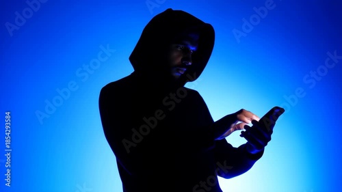 A hooded figure interacts with a smartphone against a vibrant blue backdrop. the image evokes themes of cybersecurity, digital privacy, and anonymity, capturing the essence of the modern tech-driven w