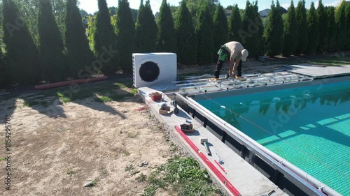 Worker Installs Equipment Next to a Swimming Pool in a Sunny Location