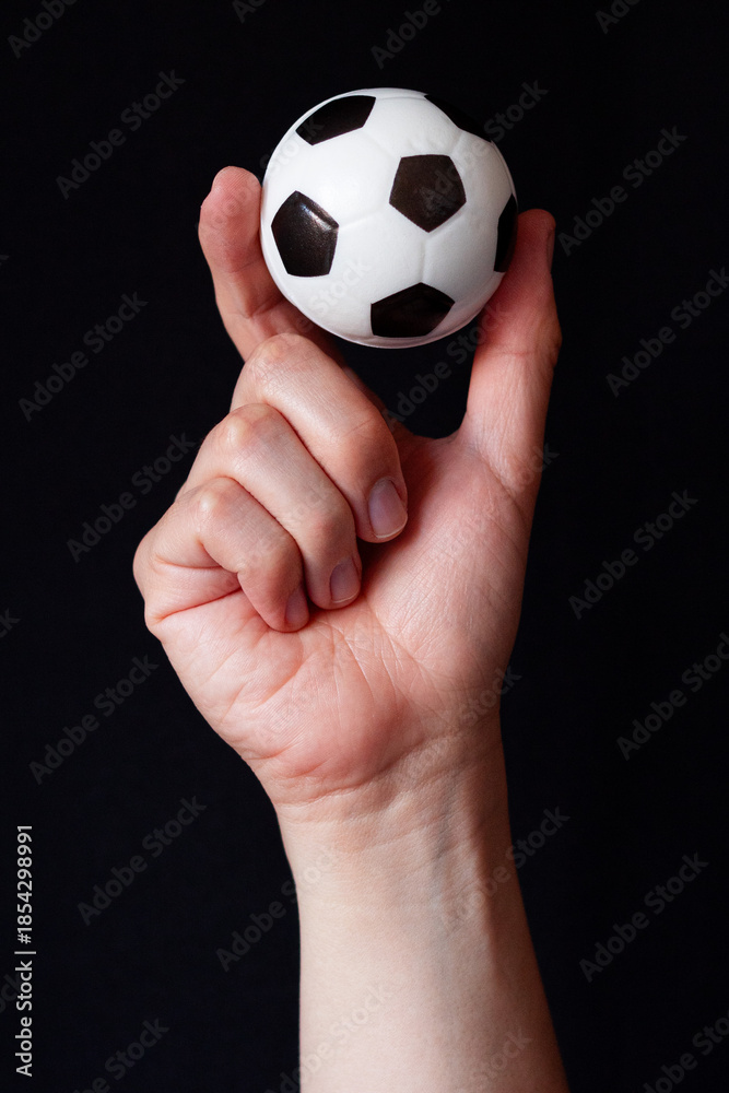 Fototapeta premium Soccer ball held with two fingers on a black background, symbolizing emotional control and soccer as daily medicine. Squeezable foam stress ball.