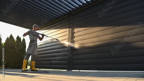 Pressure Washing a Black Fence With a Power Washer in the Backyard During Daytime