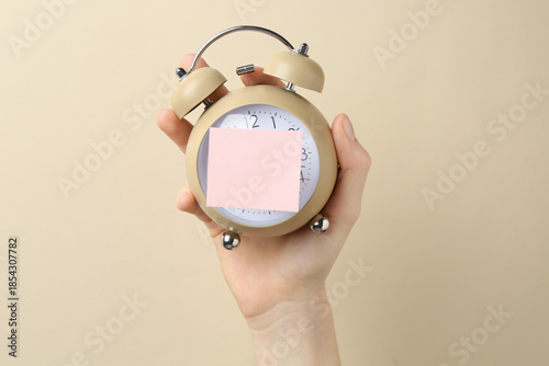 Woman with sticky note and alarm clock on beige background, closeup