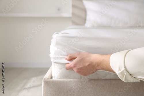 Foto Man putting bed sheet on mattress indoors, closeup