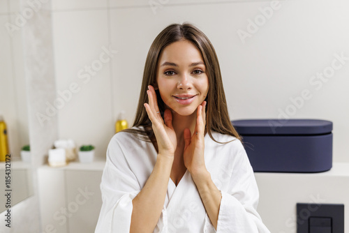 Photos Pretty woman making face-lifting massage in bathroom, looking at mirror and smil