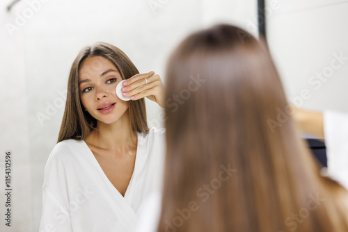 Canvas Print Beautiful young woman removing makeup with cotton pad in bathroom