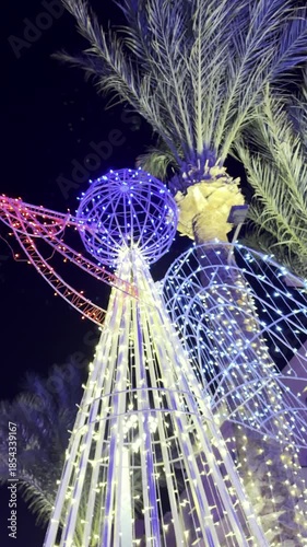Palm trees and a Christmas angel decorated with colorful garland lights at night