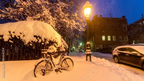 A winter scene with a snow-covered bicycle and buildings lit by streetlights at dusk.