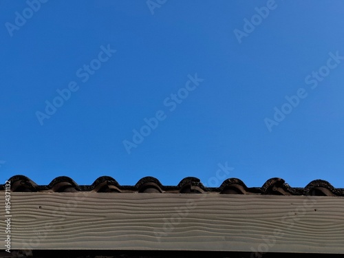 Foto Close up of dark brown clay roof tiles and cream fiber cement fascia board with wood texture under a bright clear blue sky