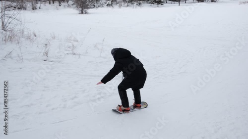 Teenager girl is snowboarding on the snow mountain. Cute happy children having fun outdoors in winter on sledge. Snowboarding offers a chance to experience winter atmosphere. Family winter time. 